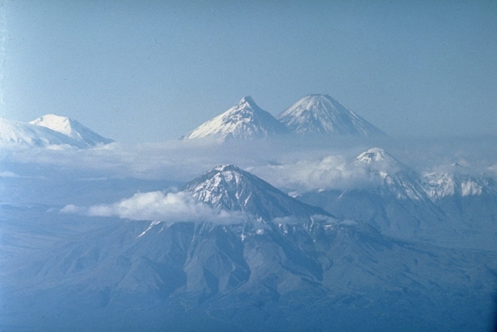 This photo looks north along the cluster of large edifices forming the Klyuchevskaya volcano group. Udina (foreground) and Zimina (middle right) are Holocene cones. Kamen (top center) and Klyuchevskoy (top right) are the far-background. Ushkovsky volcano (top left) lies at the NW end of the volcanic group. Bezymianny is hidden below clouds beside Kamen.  Photo by Oleg Volynets (Institute of Volcanology, Petropavlovsk).