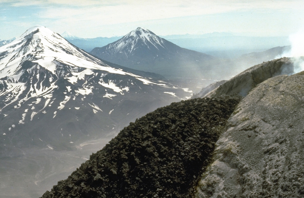 Zimina (left) and Udina (center) are shown here beyond a dark-colored lava flow from an active 1990 Bezymianny lava dome. Both Udina and Zimina encompass two edifices, only one of each are visible in this photo. Photo by Dan Miller, 1990 (U.S. Geological Survey).