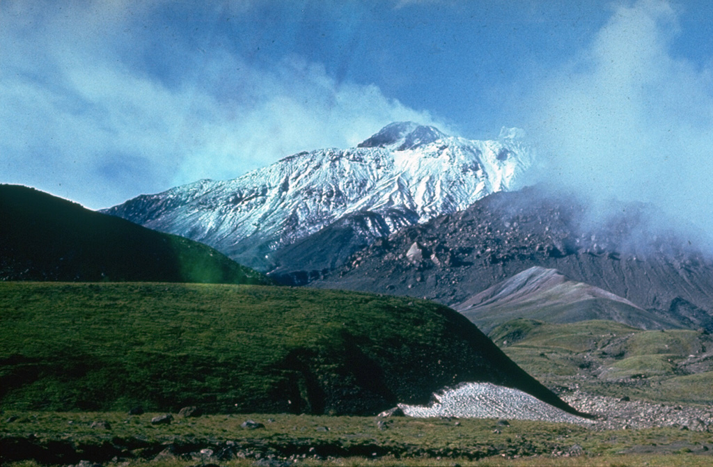 The south flank of Bezymianny contains several lava domes of Holocene age, one of which forms the unvegetated mass partly obscured by clouds to the left. The mostly snow-free summit lava dome rises above the south rim of the 1956 crater. The tip of Kamen is visible above the high point on the western crater rim to the left. Photo by Yuri Doubik (Institute of Volcanology, Petropavlovsk).