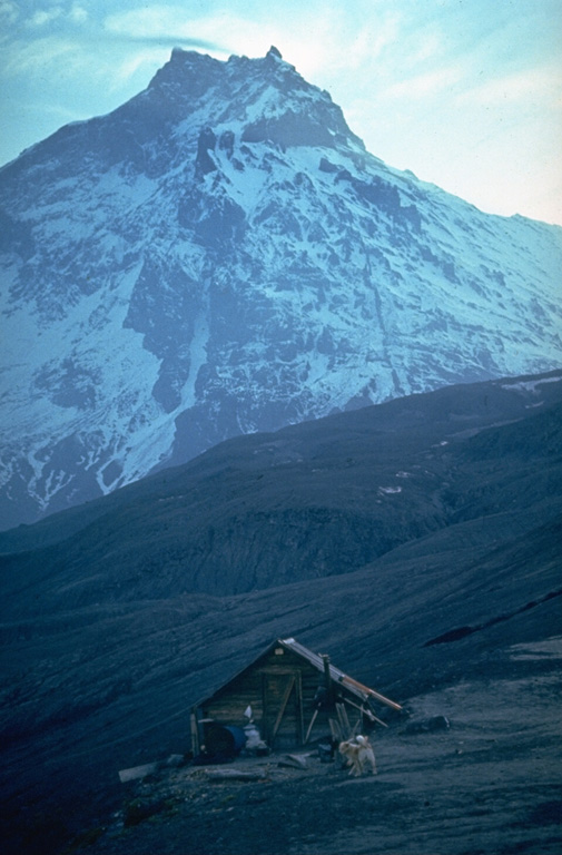 Rugged Kamen towers above a volcanological field station on the flank of Bezymianny. The ridge in the center of the photo is the southern rim of a scarp created by a massive volcanic landslide about 1,200 years ago. Collapse of the summit created a massive debris avalanche that reached more than 30 km to the east. The sheer landslide headwall reaches 3 km above its base. Photo by Yuri Doubik (Institute of Volcanology, Petropavlovsk).