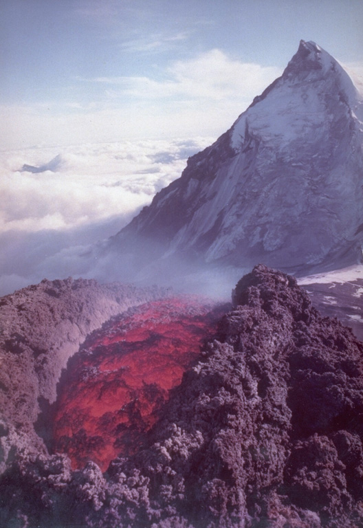 Lava extrudes from a vent on the SE flank of Klyuchevskoy volcano in 1988 with Kamen volcano in the background. Long-term activity at Klyuchevskoy has produced both explosive eruptions and lava effusion, taking place from vents at the summit and on the flanks. The steep eastern flank of Kamen resulted from collapse of the summit about 1,200 years ago, resulting in a massive debris avalanche that traveled approximately 30 km. Photo courtesy of Anatolii Khrenov, 1988 (Institute of Volcanology, Petropavlovsk).
