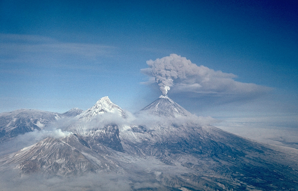 An ash plume erupts from the summit of Klyuchevskoy on 16 February 1987. Long-term activity includes both explosive and effusive activity from summit and flank vents. This view from the south shows Bezymianny producing a small plume at the lower left, Kamen at the left center, and the broader Ushkovsky on the left horizon. Photo by Alexander Belousov, 1987 (Institute of Volcanology, Kamchatka, Russia).