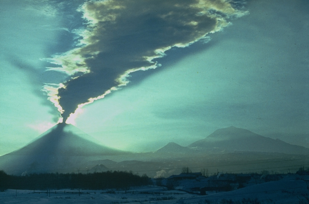 An ash plume from Klyuchevskoy in 1979 is dispersed in front of the sun in this view looking from the SW. This was part of a dominantly explosive eruption that took place from August 1977 until 1980. The eruption concluded with explosive activity and lava effusion from a flank vent during 5-12 March 1980. Ushkovsky is to the right, with the small Sredny cone in the center. Photo by Yuri Doubik, 1979 (Institute of Volcanology, Petropavlovsk).