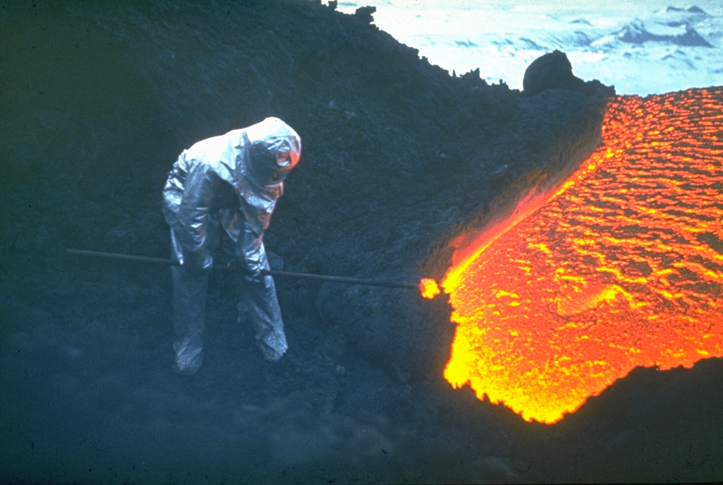 A volcanologist from the Institute of Volcanology in Petropavlovsk, shielded from the intense heat in a reflective suit, extracts a glowing sample of lava from a flank vent of Klyuchevskoy volcano in 1983. Geochemical analysis of lava samples is used to understand the eruption dynamics and the magmatic history of the volcano. Eruptions of flank and summit lava flows are common here. Protective clothing is always needed when working on active volcanoes, but sampling at lava flows such as this is rare. Photo by A. Ozerov, 1983 (courtesy of Yuri Doubik, Institute of Volcanology, Petropavlovsk).