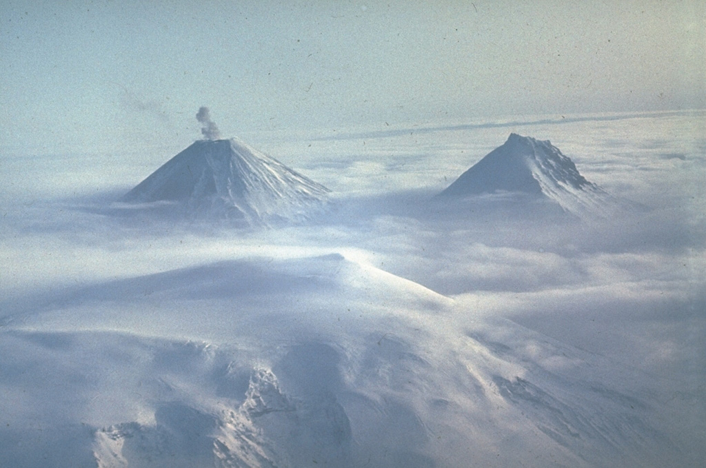 Clouds drape the margins of the glacier-covered summit caldera of Ushkovsky (Plosky) volcano in the foreground. Two of the highest volcanoes in Kamchatka, Klyuchevskoy (left) and Kamen (right) rise above the layer of clouds to the SE. A small ash plume drifts above the summit of Klyuchevskoy, one of Kamchatka's most active volcanoes.  Photo by Yuri Doubik (Institute of Volcanology, Petropavlovsk).