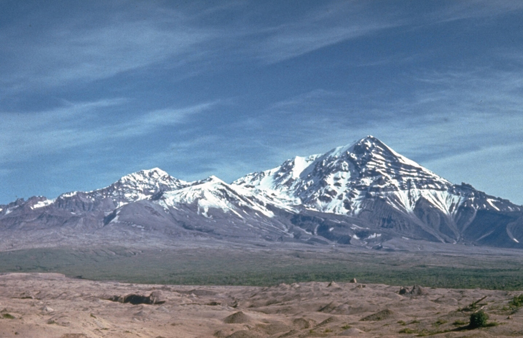 Sheveluch has undergone several large flank collapse events to shape the edifice we see today. The frequent collapses of lava-dome complexes have produced numerous debris avalanches whose deposits cover much of the area south of the volcano. The light-colored hummocky deposits in the foreground were produced during the latest collapse in 1964. Photo by Kamchatka Volcanic Eruptions Response Team (courtesy of Dan Miller, U.S. Geological Survey).