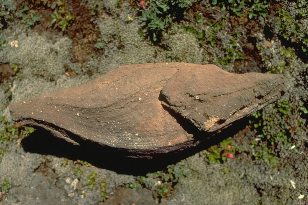 This roughly 50-cm-long volcanic bomb, erupted from Westdahl volcano in the Aleutians, is known as a spindle bomb.  Molten masses of magma that are blown out of the crater commonly become aerodynamically rounded into a spindle shape as they are hurled through the air.  Some bombs are still partially molten and become deformed when they impact onto the ground. Copyrighted photo by Katia and Maurice Krafft, 1978.
