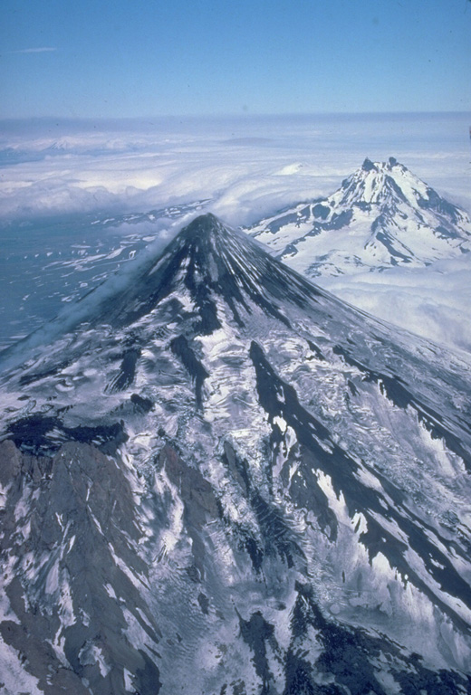 Despite its extensive glacial cover, Shishaldin volcano maintains its symmetrical profile because of frequent eruptions.  Aa lava flows, erupted from summit and satellitic vents, spread over the NW flank, the location of more than 2 dozen pyroclastic cones.  The dominantly basaltic volcano is the highest peak in the Aleutian Islands.  The rugged, dissected Isanotski volcano rises to the east behind Shishaldin. Copyrighted photo by Katia and Maurice Krafft, 1978.
