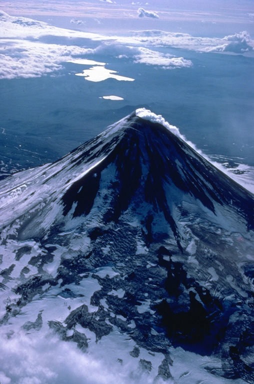 An almost constant steam plumes pours down the north flank of Shishaldin volcano, the highest in the Aleutian Islands.  The symmetrical volcano is the most prominent landmark on Unimak Island and is referred to by the Aleut Indians as Sisquk, meaning "mountain which points the way when I am lost."  A large monogenetic cinder cone field is found on the NW flank of the basaltic volcano.  The two large lakes in the distance are within Fisher caldera, a low-lying volcanic structure to the SW. Copyrighted photo by Katia and Maurice Krafft, 1978.