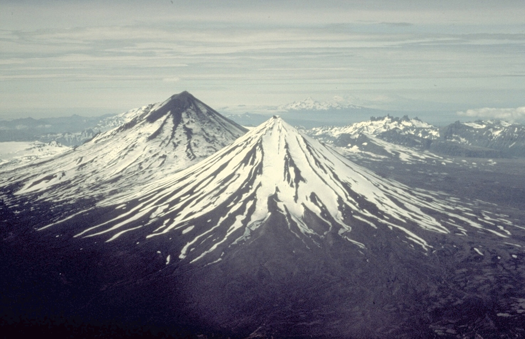 Pavlof Sister (center) and Pavlof (upper left) are twin stratovolcanoes whose summits are only 5 km apart.  A low saddle about 1100-m high separates the conical volcanoes.  They are the most prominent features along a NE-SW-trending line of vents that extends from Emmons Lake caldera, which is behind 2519-m Pavlof volcano in this view from the NE, to 2142-m Pavlof Sister volcano. Copyrighted photo by Katia and Maurice Krafft, 1978.