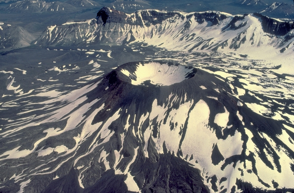 Vent Mountain, a post-caldera volcano that rises 450 m above the caldera floor, is the largest of a variety of volcanic features on the floor of the 10-km-wide caldera.  In addition to Vent Mountain, the most prominent post-caldera features are Half Cone, on the NW side and a 1931 vent near the west rim.  Lava flows, tuff cones, maars, cinder cones, and lava domes are all found within Aniakchak caldera.  This view from the SW shows the east caldera rim, with The Gates, a steep-walled notch in the east rim, at the upper left. Copyrighted photo by Katia and Maurice Krafft, 1978.