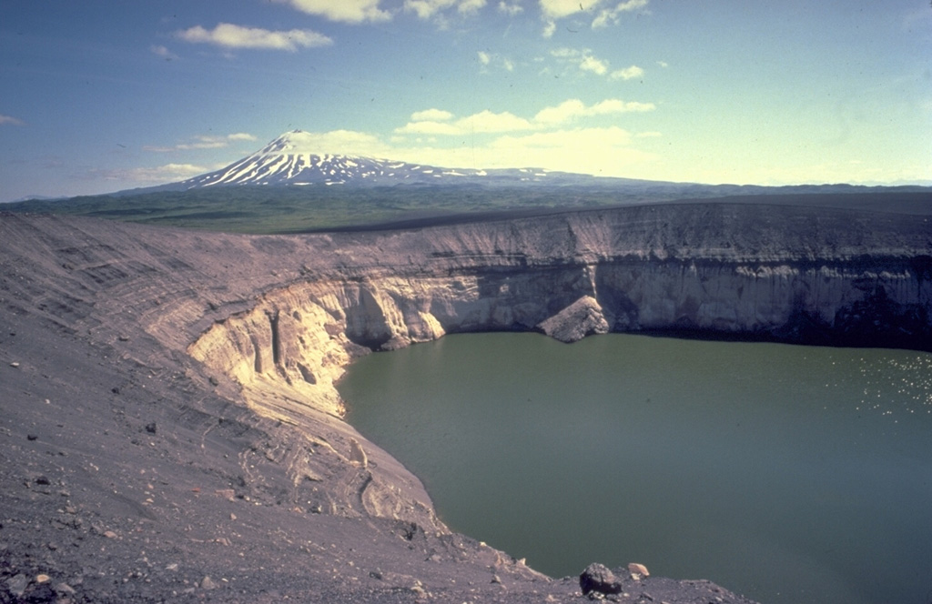 The Ukinrek Maars were formed during an eruption in 1977 at a Bering Sea lowland area without previous volcanic activity.  Powerful phreatomagmatic explosions formed the 170-m-wide West Maar and 300-m-wide East Maar.  The maars were named from the Yupik Eskimo words for "two holes in the ground."  Late in the 10-day-long eruption a lava dome formed in East Maar, seen here from the NW rim with Peulik volcano in the background.  The dome is now submerged beneath a 60-m-deep lake. Copyrighted photo by Katia and Maurice Krafft, 1978.