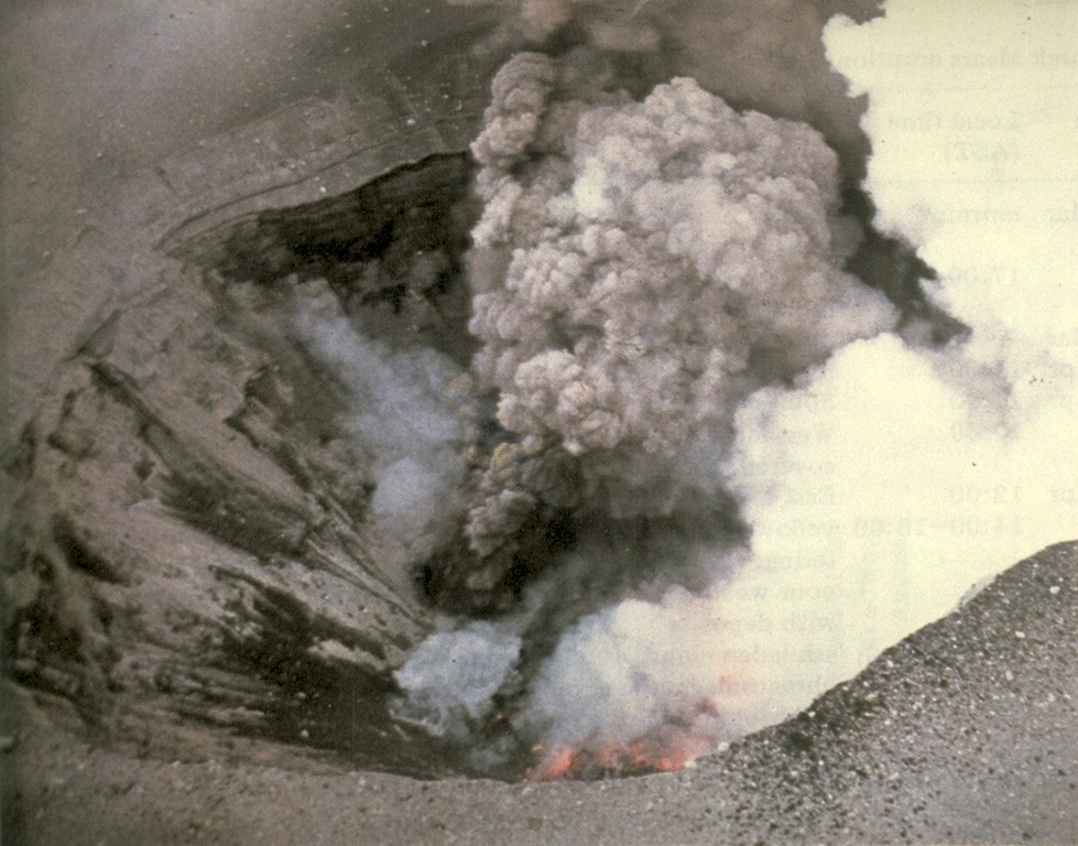 An aerial view into East Maar on 3 April 1977 shows incandescent lava on the floor of the crater and a small vent above it that is producing an ash plume. The 1977 eruptions of Ukinrek Maars began on 30 March at West Maar, which formed during the first three days of the eruption. East Maar formed during the next seven days at a location 600 m E. A lava dome, now covered by a crater lake, formed on the floor of East Maar. Photo by Ken Parker, 1977 (Alaska Department of Fish and Game).