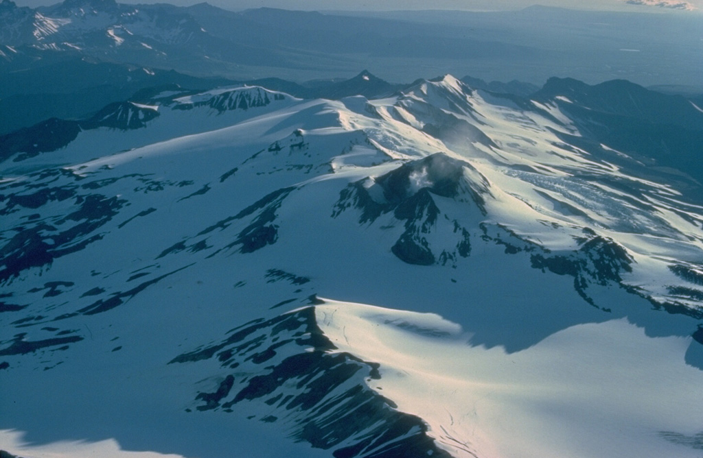 Mount Martin is a large glacier-mantled stratovolcano that anchors the SW end of NE-SW-trending chain of volcanoes cutting across Katmai National Park.  A large postglacial lava flow extends 12 km to the NW.  A 500-m-wide summit crater is largely ice-free because of strong fumarolic activity.  This 1978 view looks down the long axis of elongated Mount Martin from the NE.  Copyrighted photo by Katia and Maurice Krafft, 1978.