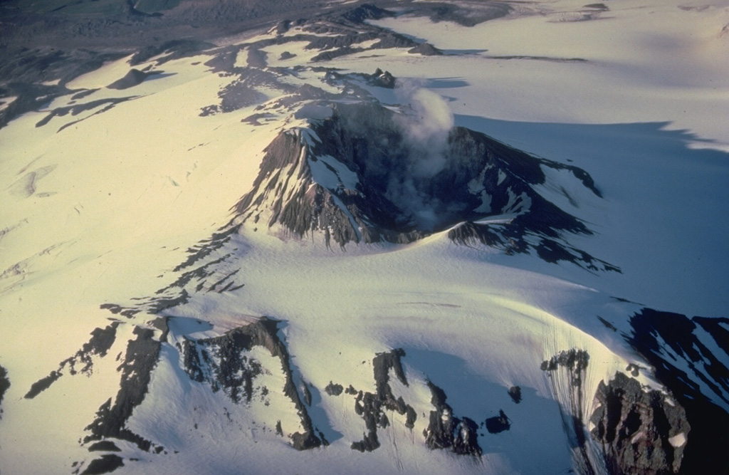 An almost-constant steam plume rises from the 500-m-wide summit crater of Mount Martin.  High heat flux at the summit keeps the crater largely free of snow and ice despite the extensive glacial cover on the rest of the volcano.  A small lake sometimes forms on the crater floor. Copyrighted photo by Katia and Maurice Krafft, 1978.