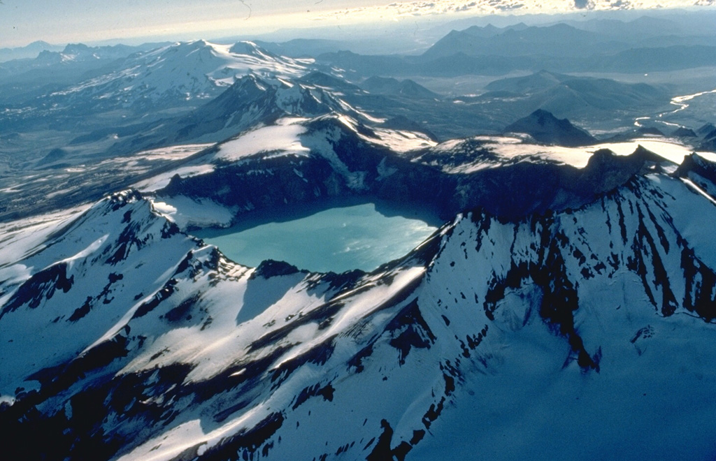 This 1978 aerial view from the NE looks down the SW-trending chain of closely spaced volcanoes in Katmai National Park.  Katmai volcano, in the foreground, is truncated by a 4.5-km-wide caldera created by collapse of the volcano in 1912 at the time of the major eruption at Novarupta volcano, 10 km to the west and below the far rim of Katmai caldera.  Beyond Katmai, in line with the 250-m-deep caldera lake, are the dark-colored peaks of the Trident complex and the broad, glacier-covered slopes of Mageik volcano. Copyrighted photo by Katia and Maurice Krafft, 1978.