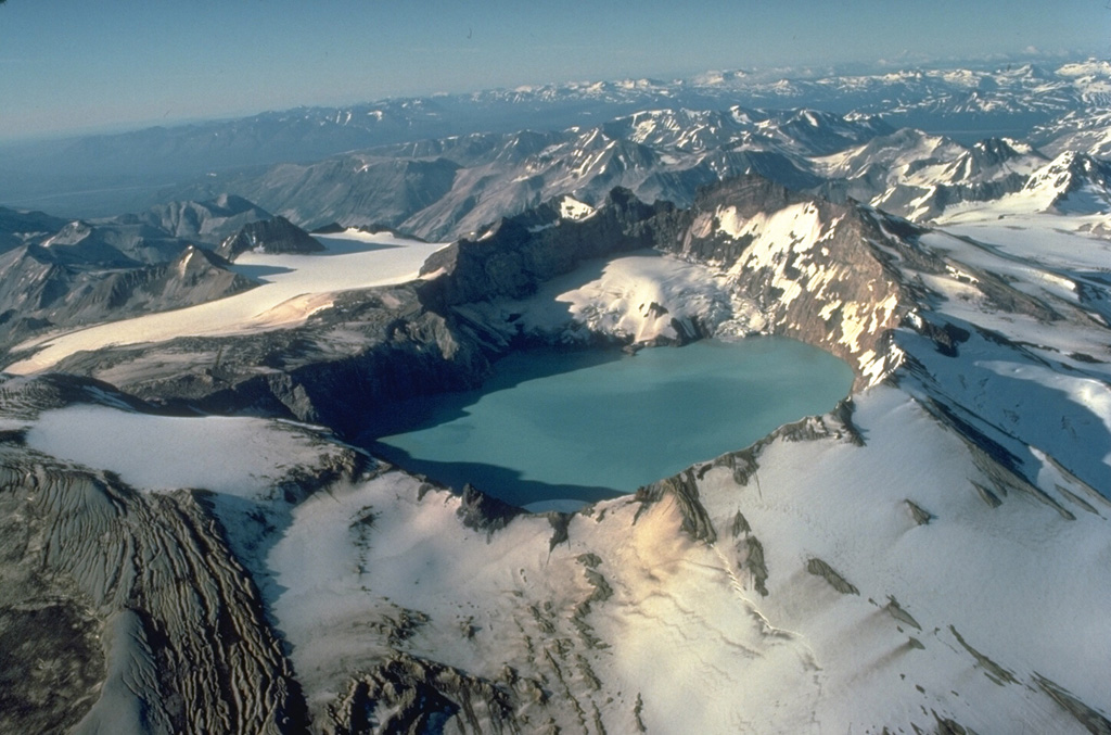 Mount Katmai, seen here from the south, is truncated by a caldera that formed in 1912 during a catastrophic eruption at Novarupta volcano, 10 km to the west.  Little eruptive activity occurred at Katmai itself during the collapse.  Prior to 1912, Mount Katmai was a 2290-m-high complex of 4 small overlapping stratovolcanoes.  The 3 x 4.5 km wide caldera is filled by a lake that was 250-m deep by 1976 and is still rising.  The small glaciers on the bench on the north caldera wall began forming shortly after the 1912 eruption.     Copyrighted photo by Katia and Maurice Krafft, 1978.