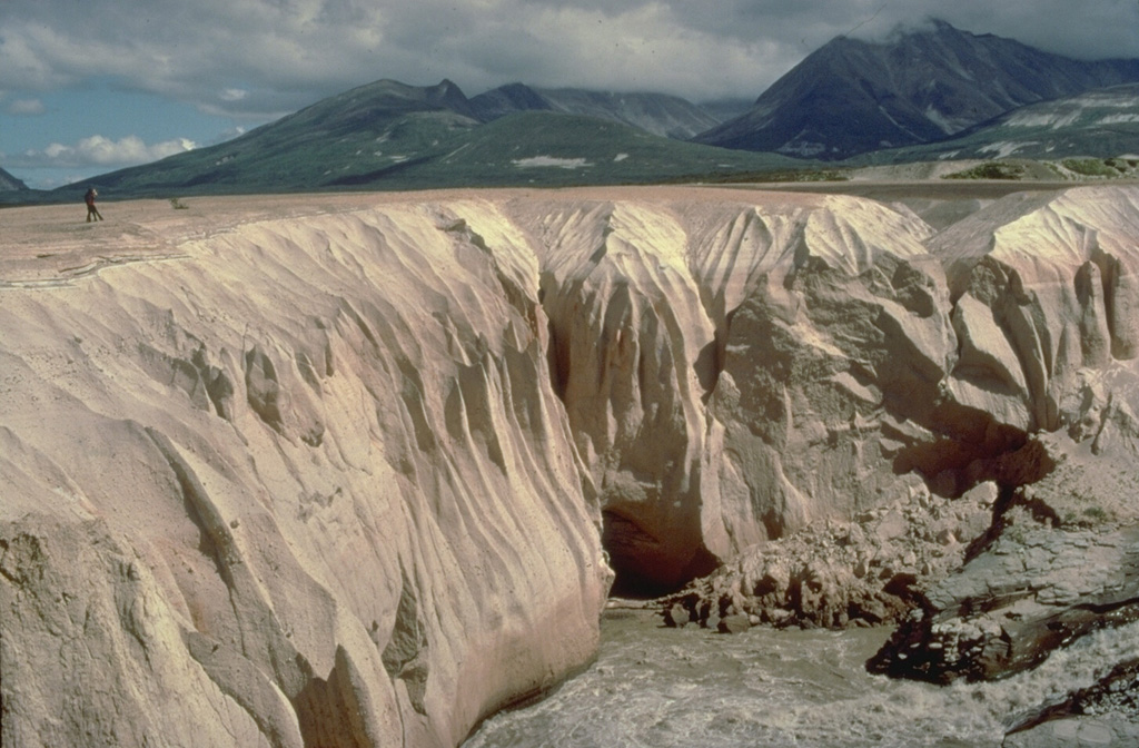 Alaska's Valley of Ten Thousand Smokes is filled with deposits from one of Earth's largest ash flows during historical time.  They were emplaced during a powerful eruption on June 6, 1912, from Novarupta volcano, a newly formed volcano 10 km west of Katmai volcano.  Stream dissection of the easily eroded, unwelded ash-flow deposit since 1912 provides a cross-sectional view of its interior.  The person standing on its surface at the left provides scale for the deposit, which covers an area of 120 cu km and has a volume 11-15 cu km. Copyrighted photo by Katia and Maurice Krafft, 1978.