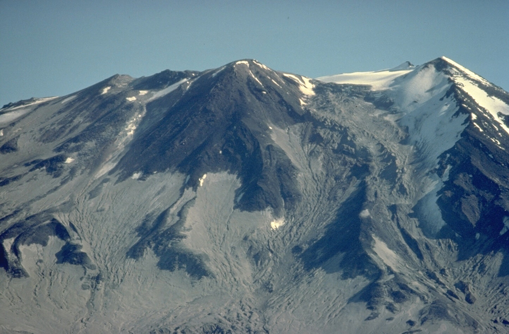 The snow-covered ridge at the right in this view from the south of Mount Griggs is the margin of a large, 1.5-km-wide breached crater formed during the early Holocene during collapse of the volcano's summit.  Remnants of the resulting debris-avalanche deposit reach WSW across the valley to Broken Mountain.  The young central cone on the center skyline filled the collapse amphitheater and displays nested craters. Copyrighted photo by Katia and Maurice Krafft, 1978.