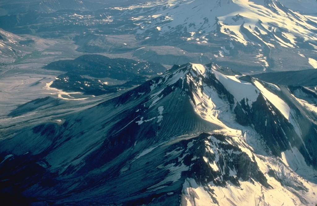 An aerial view from the east shows Mount Griggs in the foreground with the distal end of the Valley of Ten Thousand Smokes (VTTS) ash-flow deposit in the distance, forming the flat, light-colored valley floor at the upper left.  The VTTS ash flow was erupted in 1912 from Novarupta volcano; it traveled 21 km to the location shown in this photo.  Griggs volcano is the highest of a group of volcanoes in the Katmai area.  Three concentric craters are breached to the SW, the largest of which was formed by edifice collapse during the early Holocene. Copyrighted photo by Katia and Maurice Krafft, 1978.