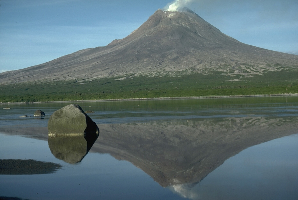 Augustine in Kamishak Bay in the southern Cook Inlet is the most active volcano of the eastern Aleutian arc. It consists of a complex of overlapping summit lava domes surrounded by an apron of volcaniclastic deposits that descend to the sea on all sides. This 1986 view from the NW shows Augustine reflected in a shallow lagoon separating the small west island from the main island. Twentieth-century eruptions have included explosive activity with pyroclastic flows and lava dome growth. Photo by Lee Siebert, 1986 (Smithsonian Institution).