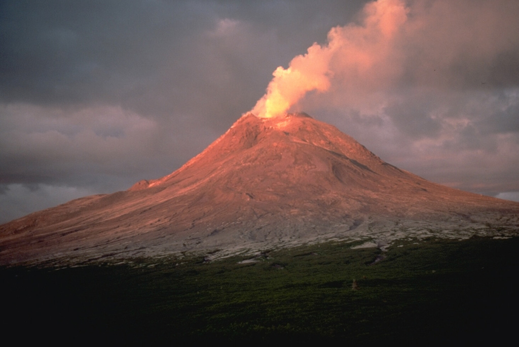 A plume rises from the degassing Augustine summit lava dome during its 1986 eruption. This June 1986 view from the NW shows ashfall and pyroclastic flow deposits covering the upper flanks, which would normally be partially covered with snow fields at this time of year. Photo by Lee Siebert, 1986 (Smithsonian Institution).