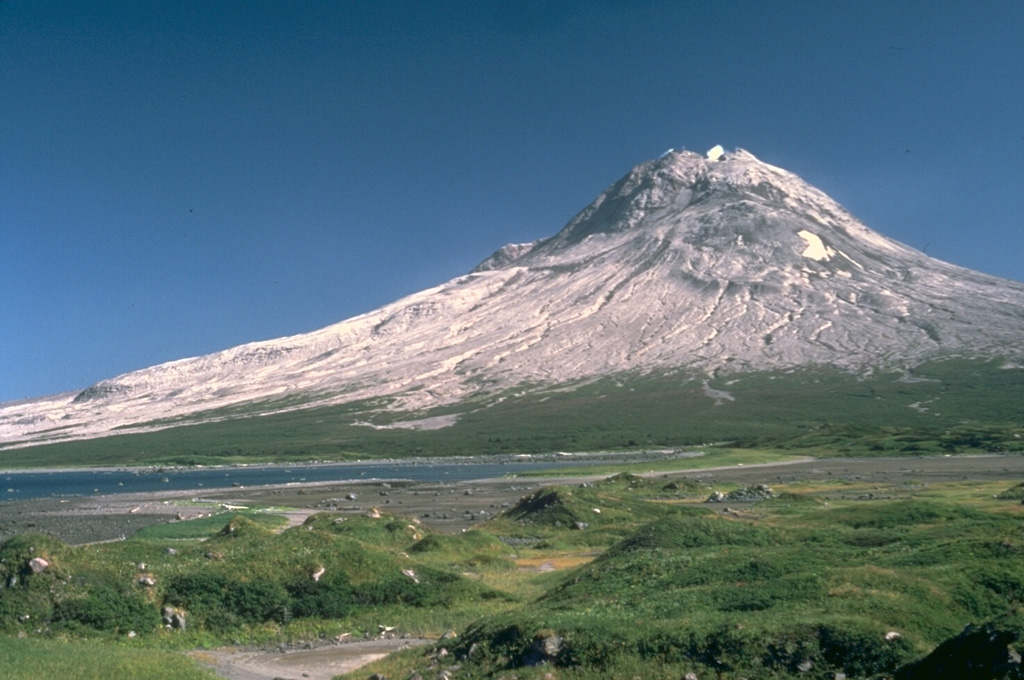 Augustine, seen here from the NW, is the most active volcano of the eastern Aleutian arc. It consists of a complex of overlapping lava domes surrounded by an apron of volcaniclastic debris that reach the sea on all sides. The hummocky deposit in the foreground is a roughly 450-year-old debris avalanche deposit, one of many that surround the island as a result of repetitive collapse of the summit lava dome. Twentieth-century eruptions included explosive activity with pyroclastic flows and lava dome extrusion. Photo by Lee Siebert, 1987 (Smithsonian Institution).
