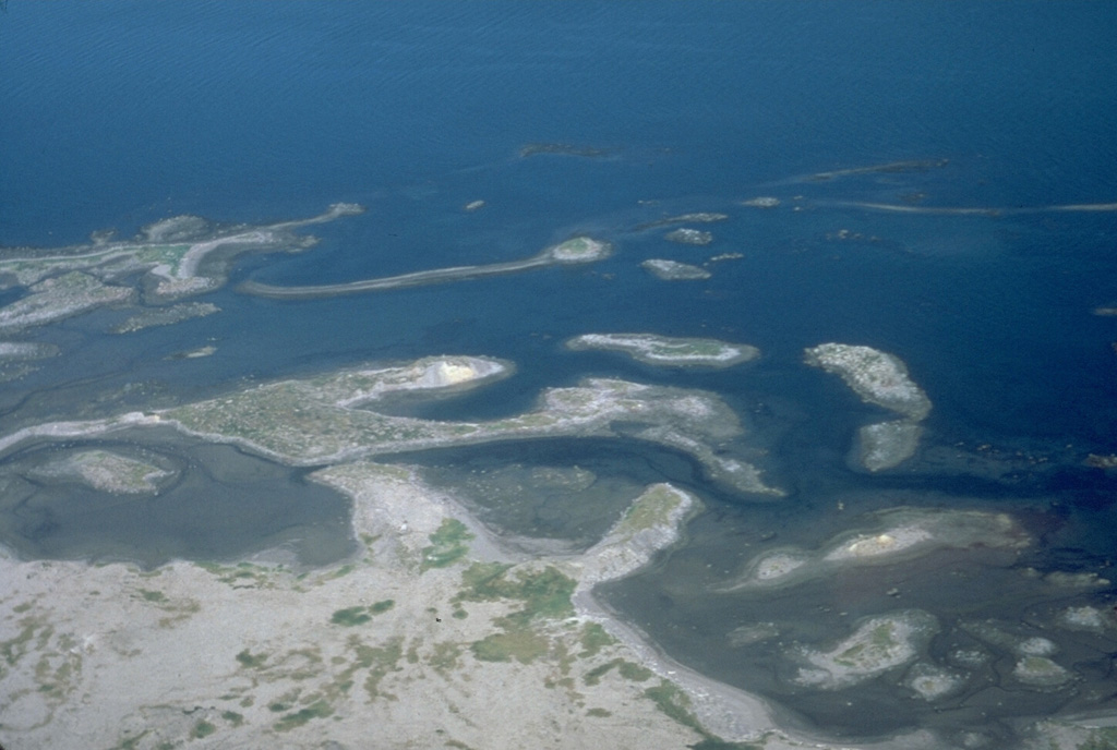 These islands and peninsulas on the north coast of Augustine formed in 1883 when collapse of the summit produced a large debris avalanche. Deposits from the highly mobile avalanche extended the island up to 2 km beyond the pre-1883 shoreline. Pyroclastic flows from that eruption also reached the new coastline and emplaced the light-colored deposits to the lower left. Photo by Lee Siebert (Smithsonian Institution).