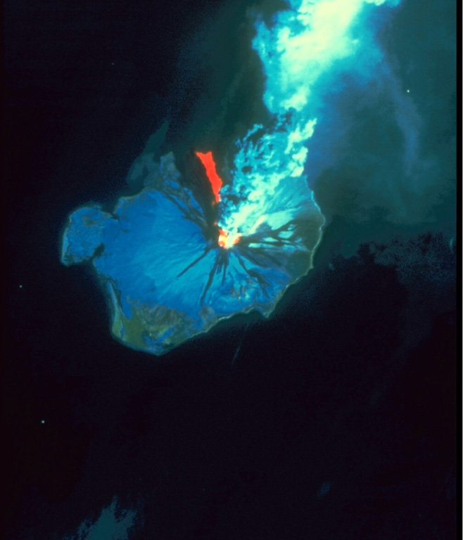 This Landsat thematic mapper image was acquired on 28 August 1986, as Augustine produced a powerful explosive eruption. An 11-km-high ash plume rises from the summit crater to the top of the false-color image. The red area in this false-color image is a hot pyroclastic flow deposit down the north flank. Snow and ice show up as shades of blue and vegetated areas along the coast are green. The dark areas descending the flanks are the paths of lahars and cooled pyroclastic flows. NASA Landsat image, 1990.