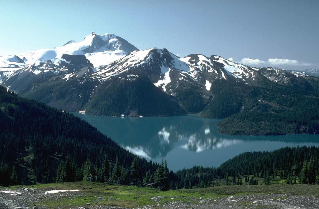 The Garibaldi Lake volcanic field consists of nine small stratovolcanoes and vents of Pleistocene to Holocene age around Garibaldi Lake, seen here with Mount Garibaldi in the background. Mount Price, in the center of the photo, is a small andesitic stratovolcano. Clinker Peak on the west flank produced two Holocene lava flows that dammed Rubble Creek at the right-hand margin of this photo, forming Garibaldi Lake. Photo by Lee Siebert, 1983 (Smithsonian Institution).