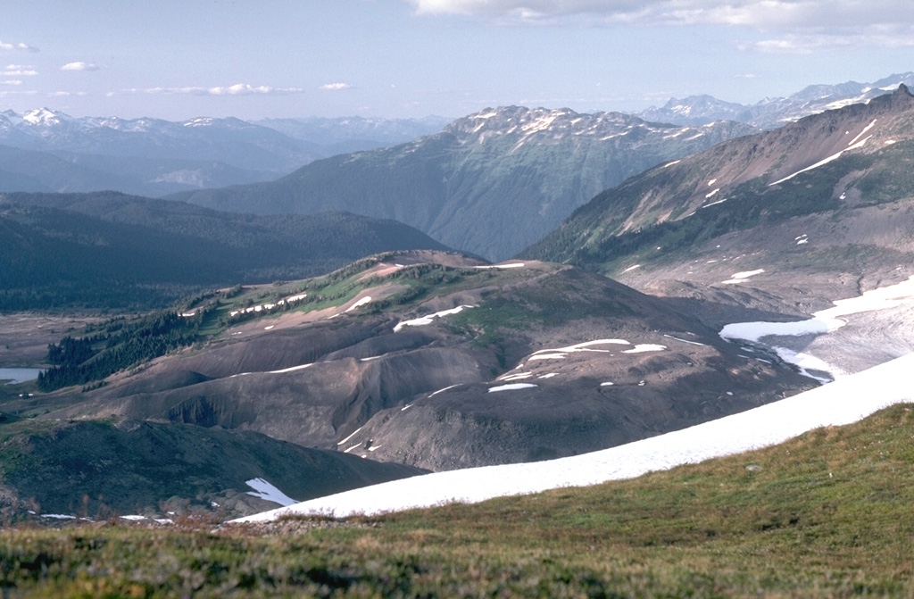 The irregular mound in the center of the photo is Cinder Cone, a late-Pleistocene cone of the Garibaldi Lake volcanic field. The cone formed during two periods of activity, the latest of which produced a lava flow down the glaciated valley to the north. Photo by Lee Siebert, 1983 (Smithsonian Institution).