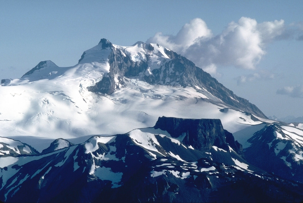 The Table, the flat-topped ridge in the foreground in front of Mount Garibaldi, is the southernmost vent of the Garibaldi Lake volcanic field. This is a tuya that formed when lava flows filled a pit melted through the continental ice sheet. A series of stacked horizontal lava flows filling the pit formed The Table.  Photo by Lee Siebert, 1983 (Smithsonian Institution).