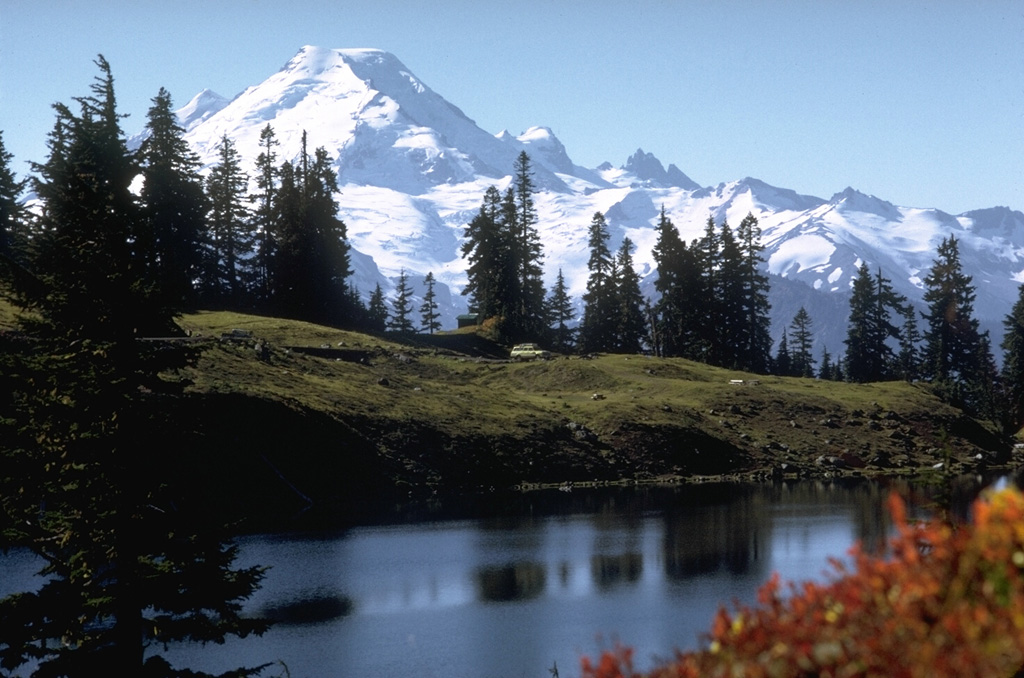 Glaciated Mount Baker is seen here from Twin Lakes to the north. Sherman Crater, the source of historical eruptions from Mount Baker, is visible on the left side between the summit and the smaller Sherman Peak. The older eroded Black Buttes volcano forms the two peaks below and to the right of the summit. Photo by Lee Siebert, 1971 (Smithsonian Institution).