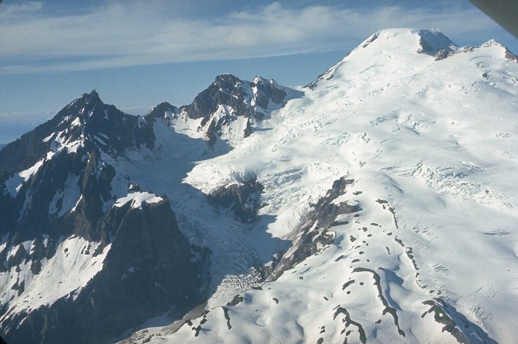 This view from the SW shows the Deming Glacier below Lincoln (left) and Colfax Peaks, which are remnants of the Pleistocene Black Buttes volcano that once stood where Mount Baker is now. Lavas from Black Buttes, which was active from about 500,000 to 300,000 years ago, dip towards Mount Baker with its flat-topped summit (upper right). Easton Glacier is on the S flank. Photo by Lee Siebert, 1972 (Smithsonian Institution).