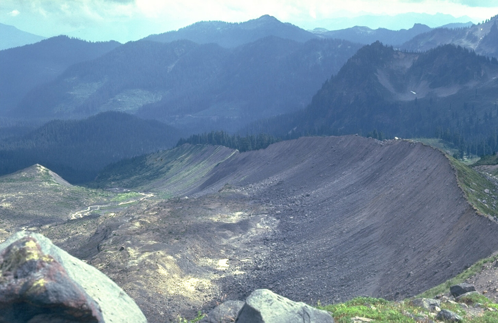 The forested scoria cone in the left of the photo is Schreibers Meadow Cone on the SE flank of Mount Baker. It erupted about 9,800 years ago, producing a scoria deposit and a lava flow that traveled 12 km to the present location of Baker Lake. The ridge in the foreground is a glacial moraine from Mount Baker known as the "Railroad Grade." Photo by Lee Siebert, 1981 (Smithsonian Institution).