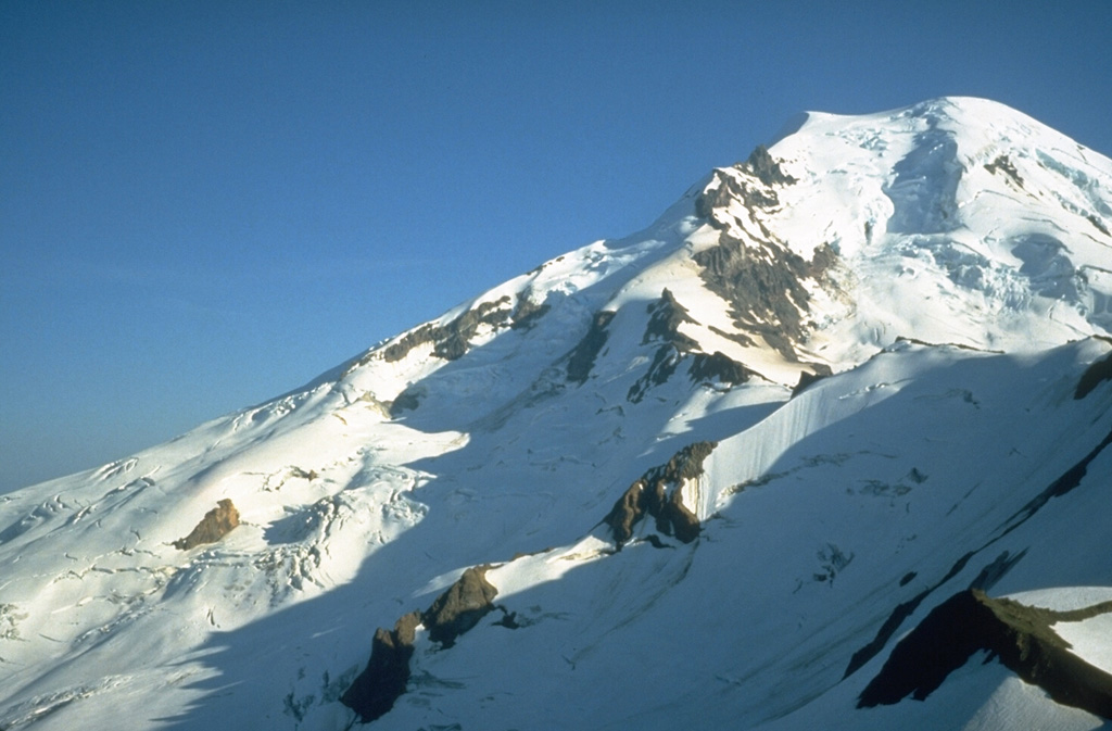 The north flank of Mount Baker towers above Cockscomb Ridge, with the Roosevelt Glacier descending from the summit. The Dole Fumarole Field on the northern flank is located below a point around halfway down the left-hand horizon, near where the shadow line on the Mazama Glacier (center) takes a sharp bend. William Henry Dorr reported vapor emission at this location in 1884 and fumarolic activity continues today. Photo by Bill Chadwick, 1981 (U.S. Geological Survey).