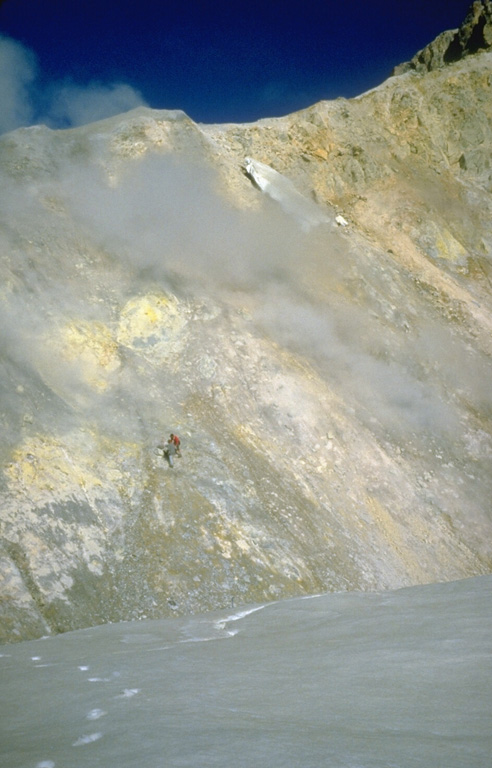 Two U.S. Geological Survey volcanologists (left center) take gas samples from a fumarole, one of many across the wall of Sherman Crater in 1981. Increased emissions had begun from Sherman Crater in 1975. The crater walls consist of brightly colored areas of hydrothermally altered rocks. Photo by Bill Chadwick, 1981 (U.S. Geological Survey).