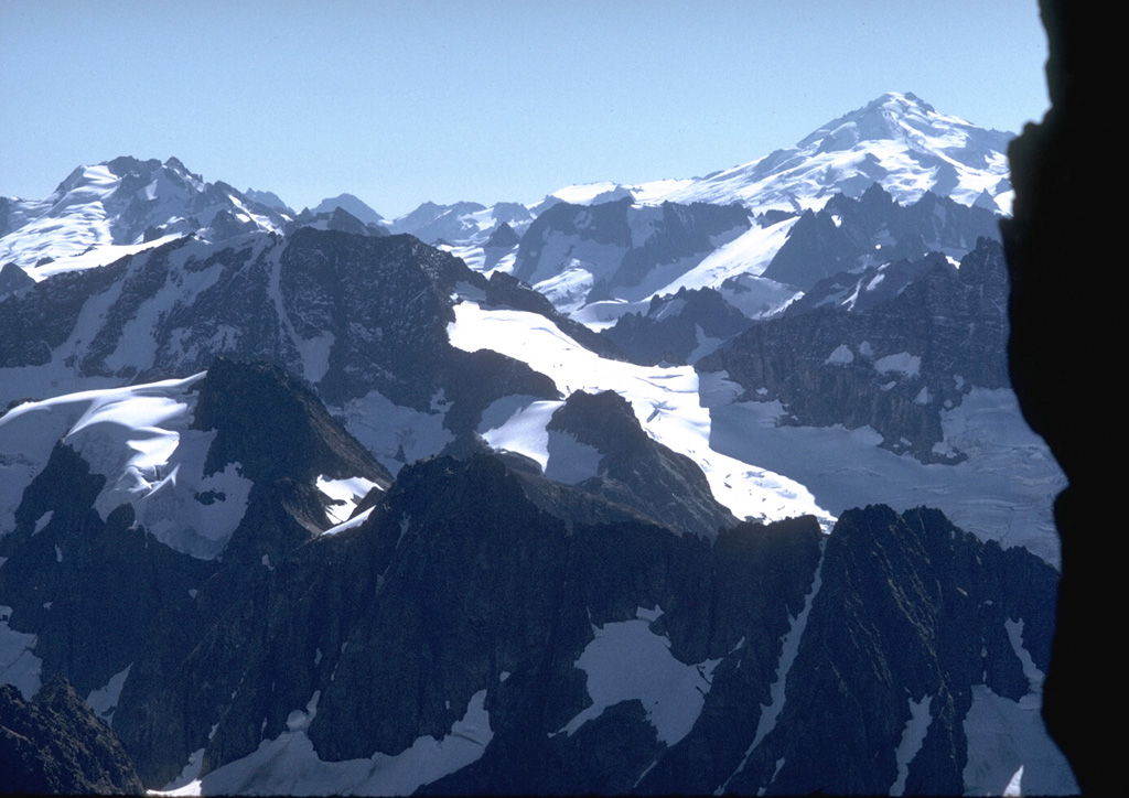 Glacier Peak, to the upper right from Forbidden Peak with Dome Peak to the upper left, rises above some of the most rugged terrain of the North Cascade mountain range.  Photo by Lee Siebert, 1971 (Smithsonian Institution).