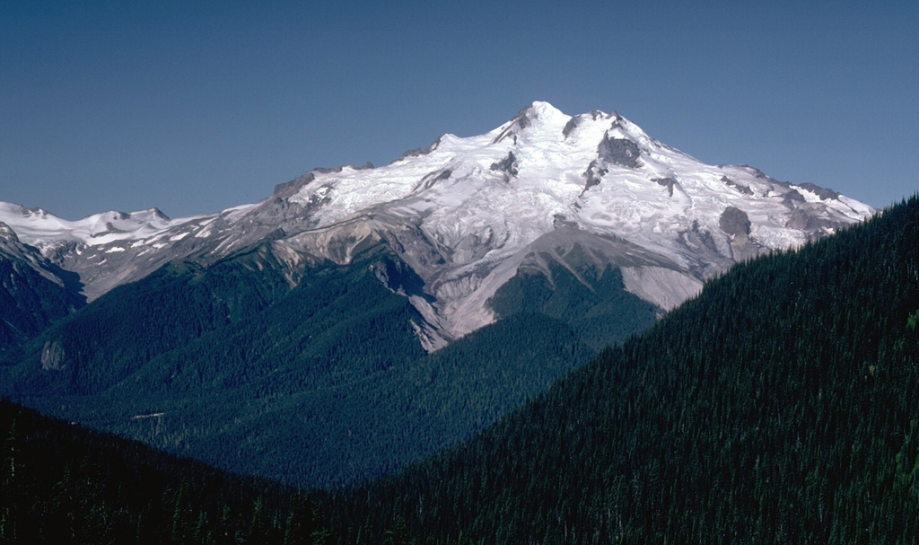 Glacier Peak rises above the forested slopes of the Suiattle River valley in this east side view from Buck Creek Pass. It has had frequent powerful explosive eruptions that deposited ash and pumice over wide areas, and produced pyroclastic flows and lahars that traveled long distances A recent eruption occurred only a few hundred years ago. Photo by Lee Siebert, 1985 (Smithsonian Institution).
