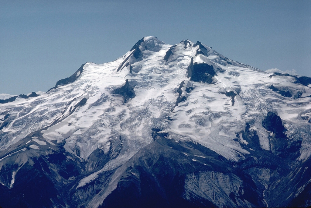 Glacier Peak, seen here from Buck Creek Pass on the west, is constructed on top of a high ridge. The eroded scarps at the base of the volcano are the head of the Suiattle River that eroded into thick pyroclastic flow and lahar deposits from recent eruptions. Photo by Lee Siebert, 1985 (Smithsonian Institution).