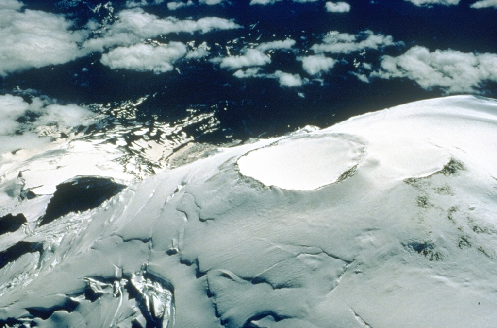 Two overlapping craters at the summit of Mount Rainier are viewed here from the NE in 1995. They are both about 400 m across and represent more recent activity after the collapse 5,600 years ago. Thermal activity formed a series of fumaroles and ice caves within the icecap filling the summit craters. Photo by Dave Wieprecht, 1995 (U.S. Geological Survey).