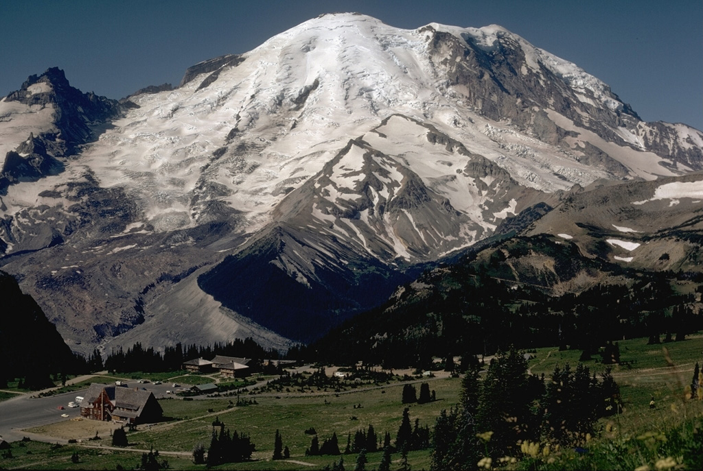 Mount Rainier rises above Yakima Park on the north side of the volcano in this 1972 photo. Emmons Glacier descends to the left from the summit within a broad valley alongside Little Tahoma Peak (far left). The valley formed when part of Mount Rainier collapsed during an eruption episode about 5,600 years ago, producing the Osceola mudflow that reached the Puget Sound area.  Photo by Lee Siebert, 1972 (Smithsonian Institution).