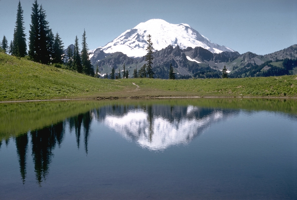 Mount Rainier rises beyond Tipsoo Lake, near Chinook Pass at the eastern end of Mount Rainier National Park. The snow-free peaks of the Cowlitz Chimneys below Rainier are composed of volcanic rocks of the Oligocene Ohanapecosh Formation which underlies the volcano. Photo by Richard Fiske, 1959 (Smithsonian Institution).