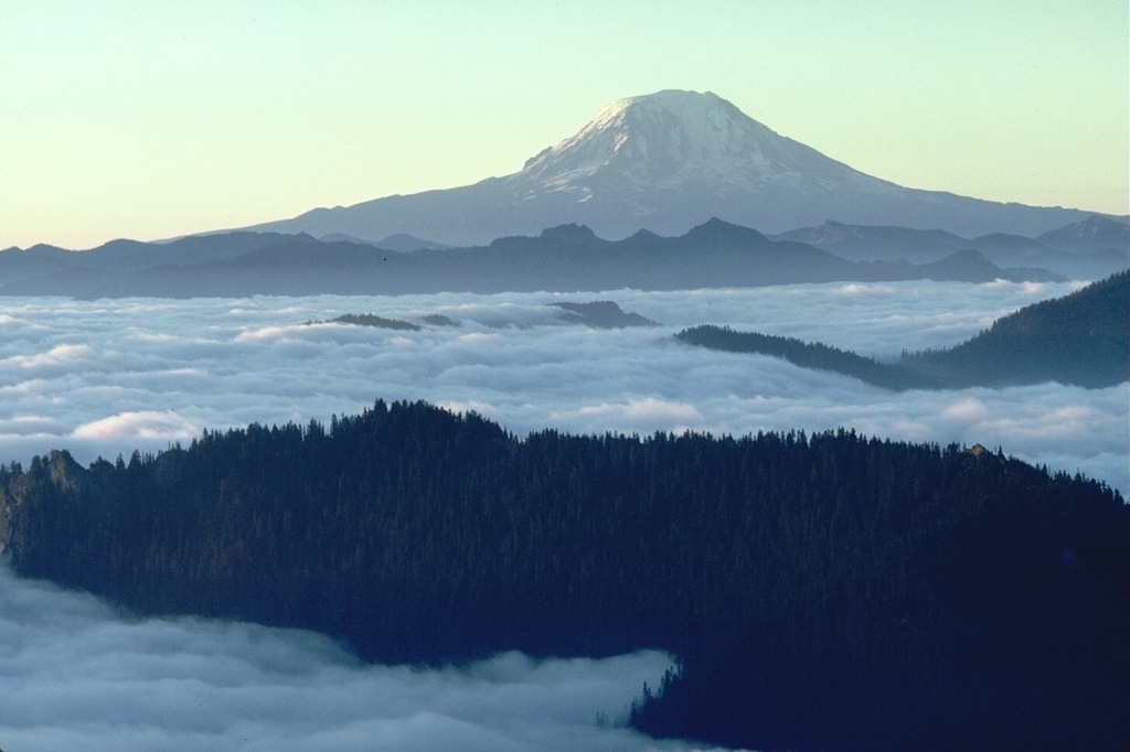 Mount Adams in the Cascade Range is seen here in 1981 from High Knob to the NW. Its base is at a lower elevation than its neighbor Mount Rainier and it has a larger volume. Numerous flank vents surround the volcano and a series of lava flows have erupted on the N, NW, S and E flanks. Photo by Lee Siebert, 1981 (Smithsonian Institution).