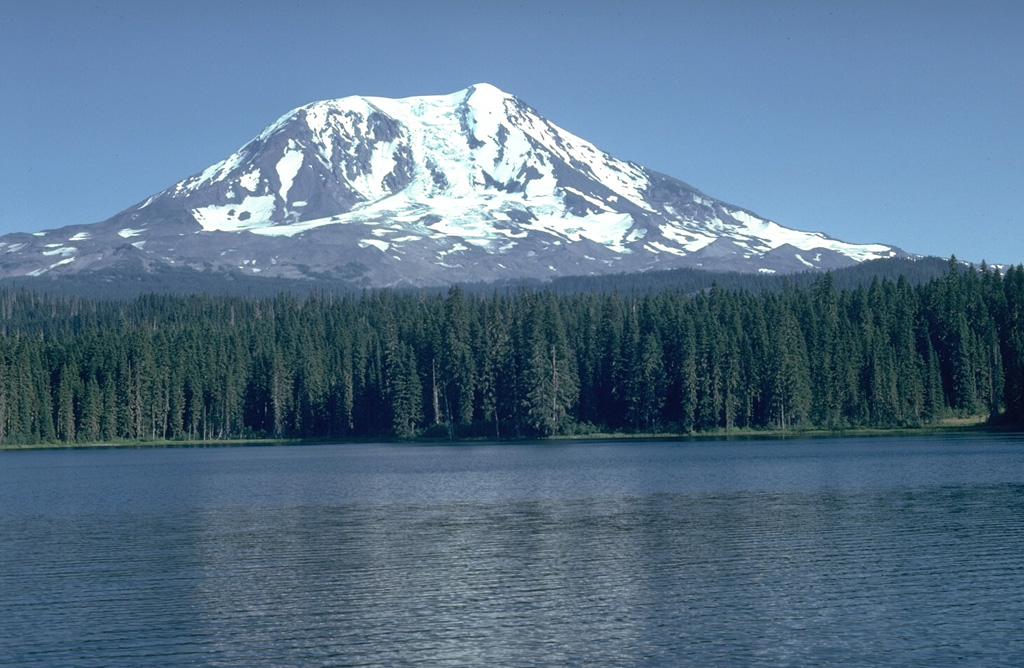 Adams Glacier descends from the summit of Mount Adams, seen here above Takhlakh Lake on the NW side. The main edifice was constructed primarily of lava flows during the Pleistocene, but flank vents produced lava flows and explosive eruptions during the Holocene. The Takh Takh Meadow lava flow originated from a vent low on the NW flank and traveled a total of 10 km, reaching several kilometers beyond the east (left) side of Takhlakh Lake. Photo by Lee Siebert, 1981 (Smithsonian Institution).