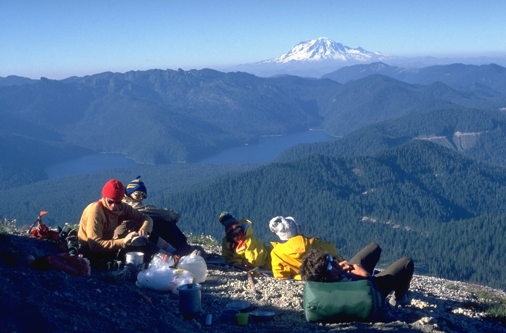 A climbing party rests on the lower N flank of Mount St. Helens in 1979, overlooking Spirit Lake and Mount Rainier. The old growth forests surrounding Spirit Lake were destroyed by the lateral blast on May 18, 1980, which covered a 600 km2 area on the north side of the volcano. Much of the area around the lake consisted of forests unaffected by logging operations prior to the 1980 eruption. Spirit Lake Lodge, owned by Harry Truman, was located W of the SW tip of the lake to the left. Photo by Lee Siebert, 1979 (Smithsonian Institution).