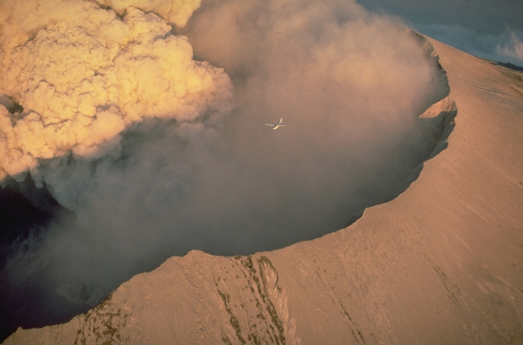 A small plane (center) flying over the west rim of the crater of Mount St. Helens provides scale for a powerful eruption column rising from the vent on the crater floor on July 22, 1980. Copyrighted photo by Katia and Maurice Krafft, 1980.