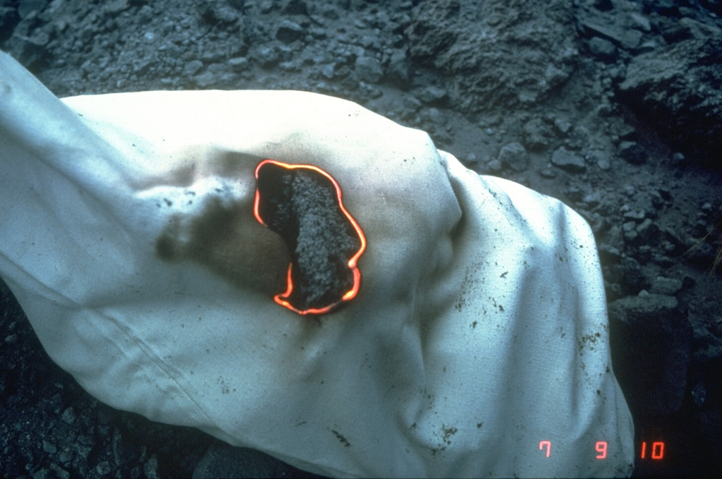 A hot rock sample collected by U.S. Geological Survey scientists during a period of lava dome growth in the crater of Mount St. Helens in September 1981 burns a cloth sample bag. Photo by Terry Leighley, 1981 (U.S. Geological Survey).