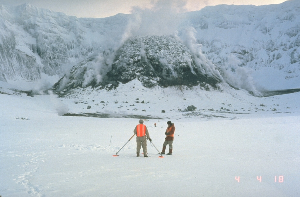 U.S. Geological Survey scientists make precision leveling measurements in the crater of Mount St. Helens in February 1982 with the steaming lava dome in the background. Repeated measurements of deformation was one of several methods used by scientists to successfully forecast later eruptions from the crater. Photo by Terry Leighley, 1982 (U.S. Geological Survey).