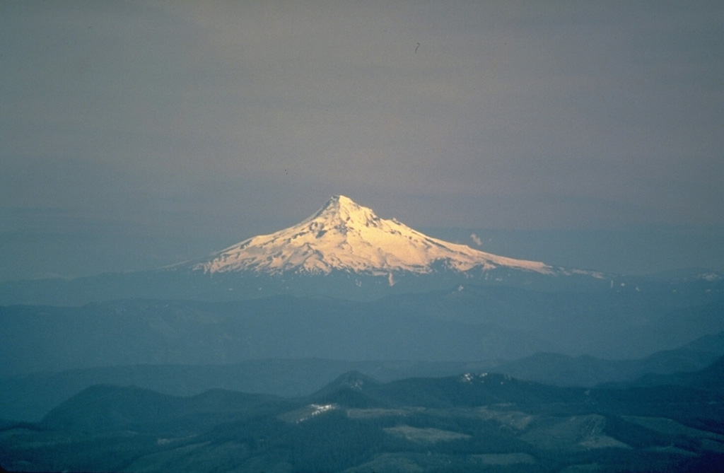 Mount Hood, seen here from the north across the Columbia River Gorge, rises above low hills of older volcanic rocks. Located only 75 km ENE of Portland, Mount Hood is near communities, infrastructure, and transportation routes, posing risk from eruptive activity and debris flows. The morphology of the summit area has been modified by flank collapse events that formed debris avalanches. Photo by U.S. Geological Survey, 1983.